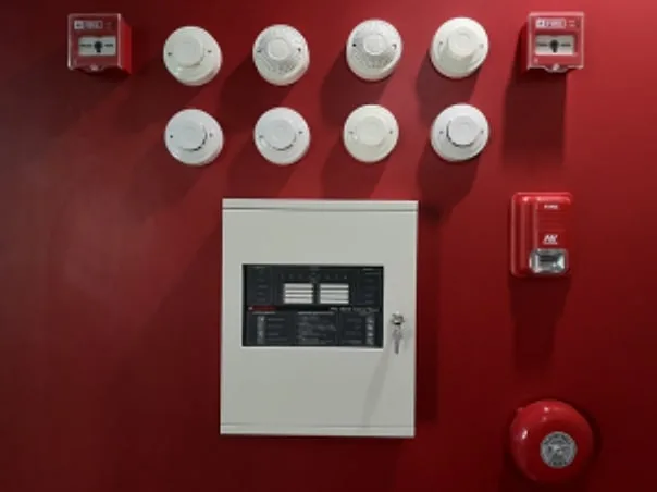 Fire alarm control panel with smoke detectors, manual call points and an alarm bell mounted on a red wall