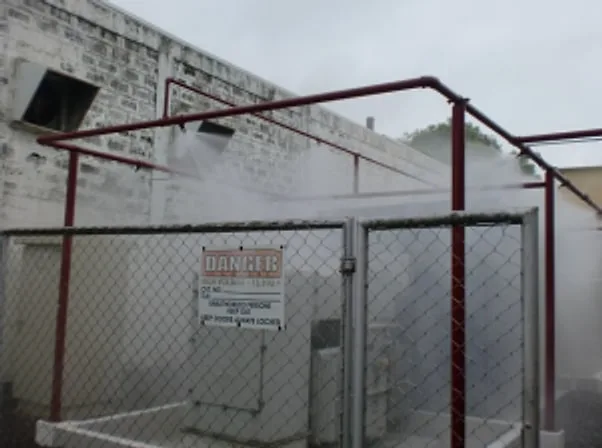 Water deluge system spraying mist over a fenced outdoor equipment enclosure