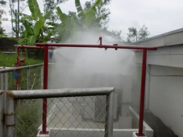 Water deluge spray test over a fenced outdoor enclosure surrounded by trees