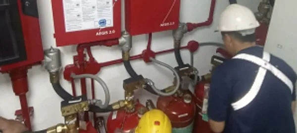 Technician in a hard hat inspecting fire suppression piping and cylinders