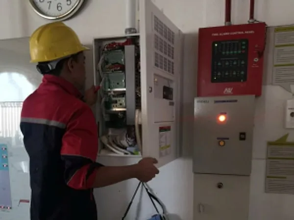 Technician in a hard hat working on an open fire alarm control panel