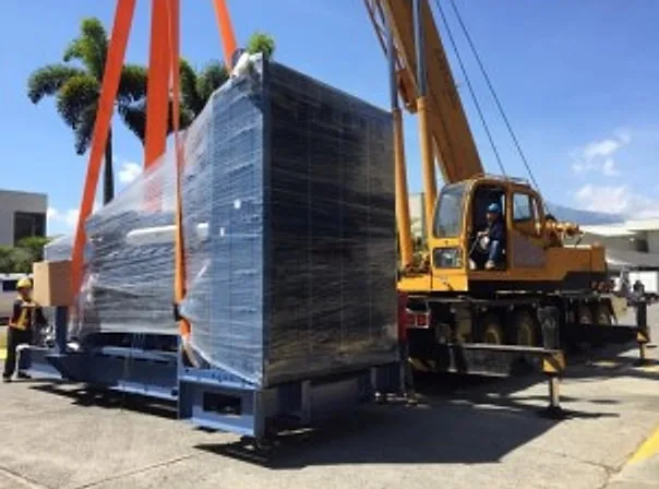 Mobile crane hoisting a plastic-wrapped generator set onto a flatbed trailer