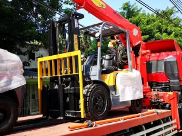 Forklift being transported on the bed of a red boom truck