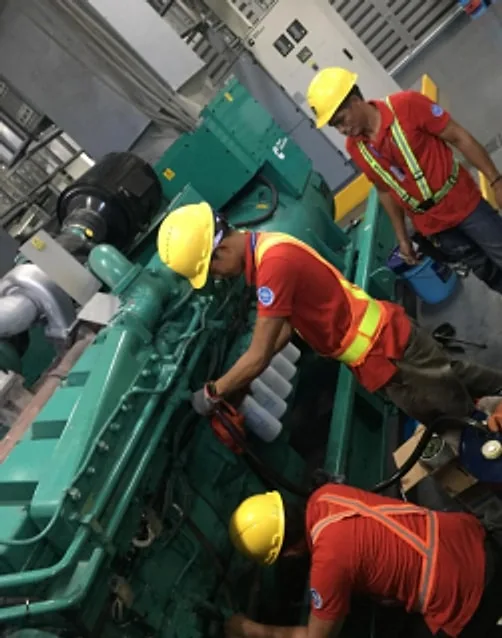 Technicians in hard hats and safety vests working on a green diesel engine