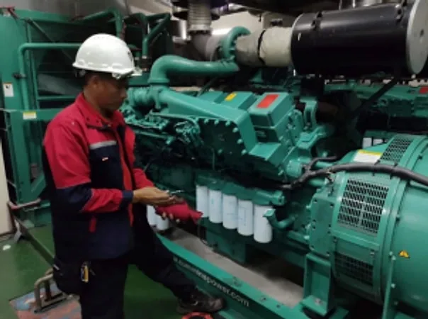 Technician in a hard hat checking a green diesel generator set engine