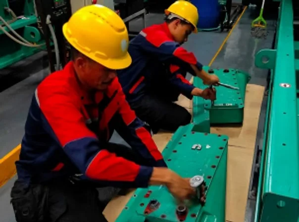 Two technicians in hard hats working on green engine components