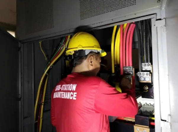 Technician in a hard hat working on wiring inside a substation panel